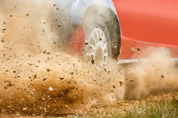 Gravel splashing from stock car drifting on dirt track.